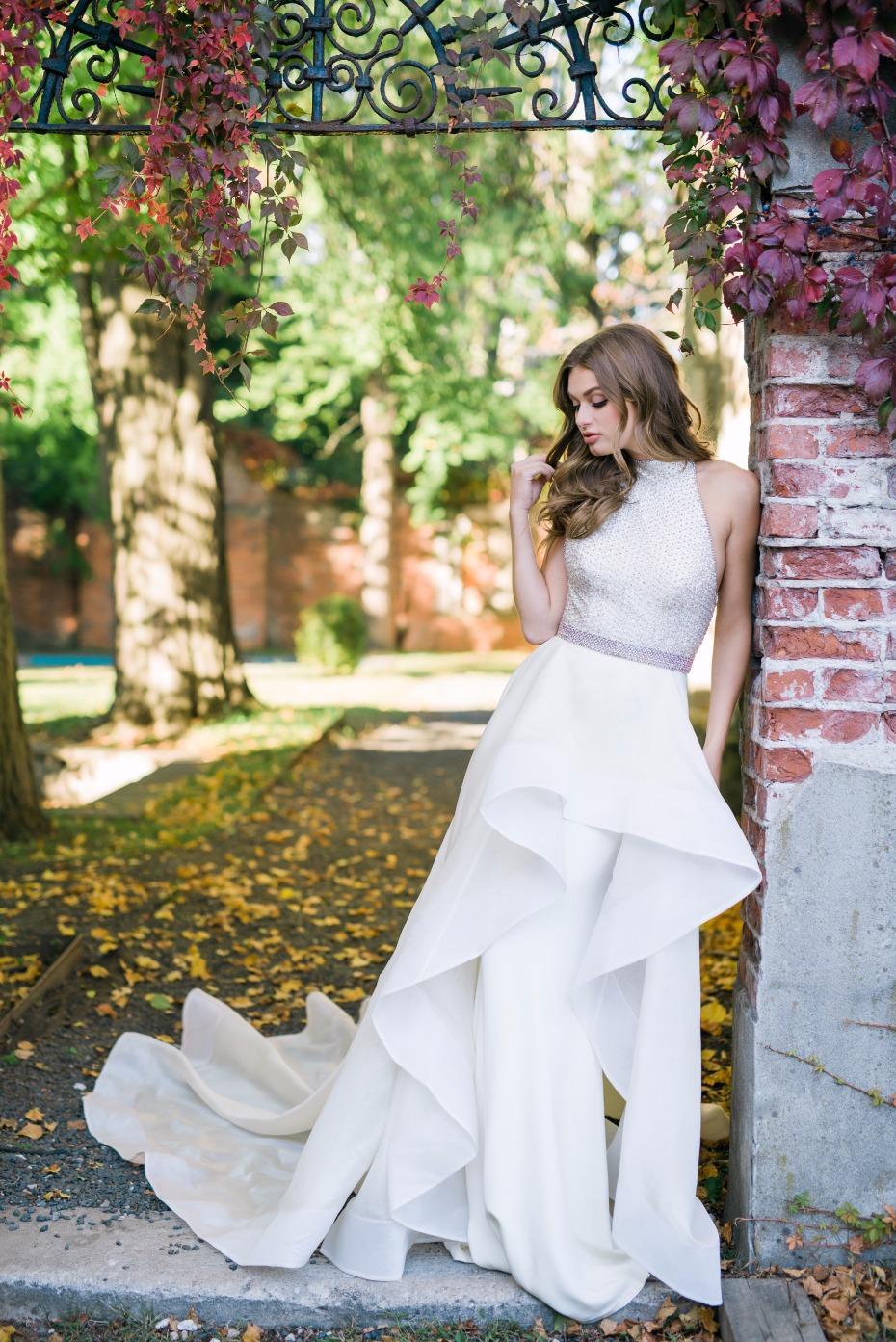 Beautiful floor length fit and flare off white bridal gown with high low skirt and train features embellished sleeveless bodice with high neckline.