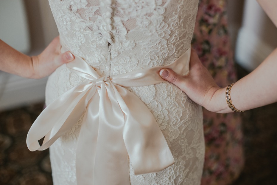 Bride standing in lace dress with hands on her hips and sash