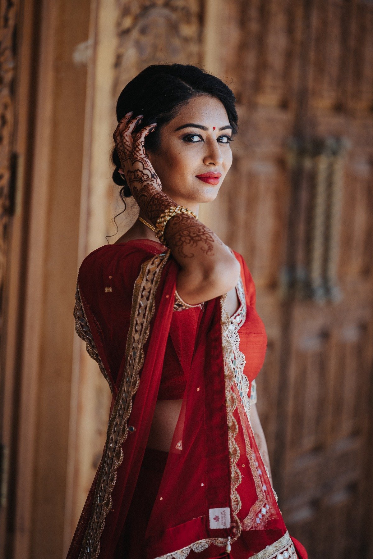 Bride holding hand with henna up to ear in traditional red dress