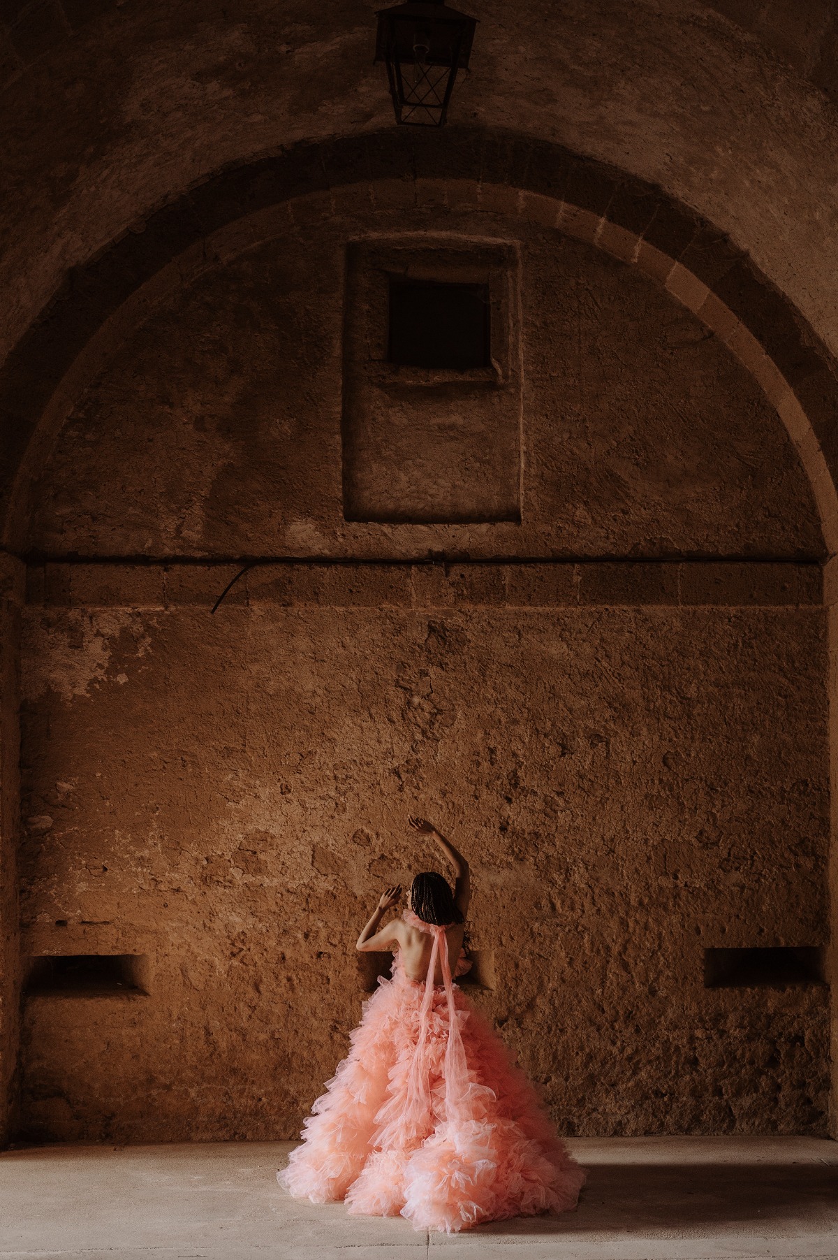 Bride in orange ruffled dress with bow neck tie facing stone wall