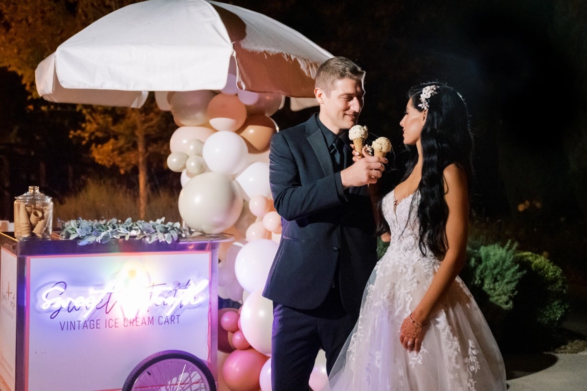 Bride and groom eating ice cream in front of a cart