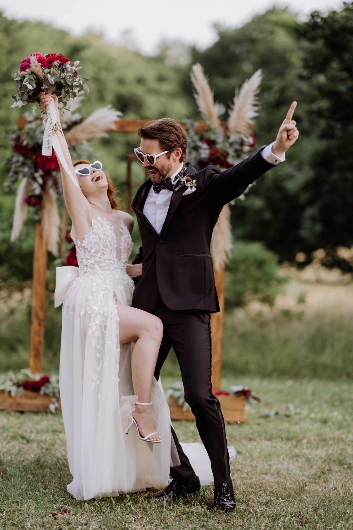 Bride and groom holding arms up wearing heart-shaped sunglasses