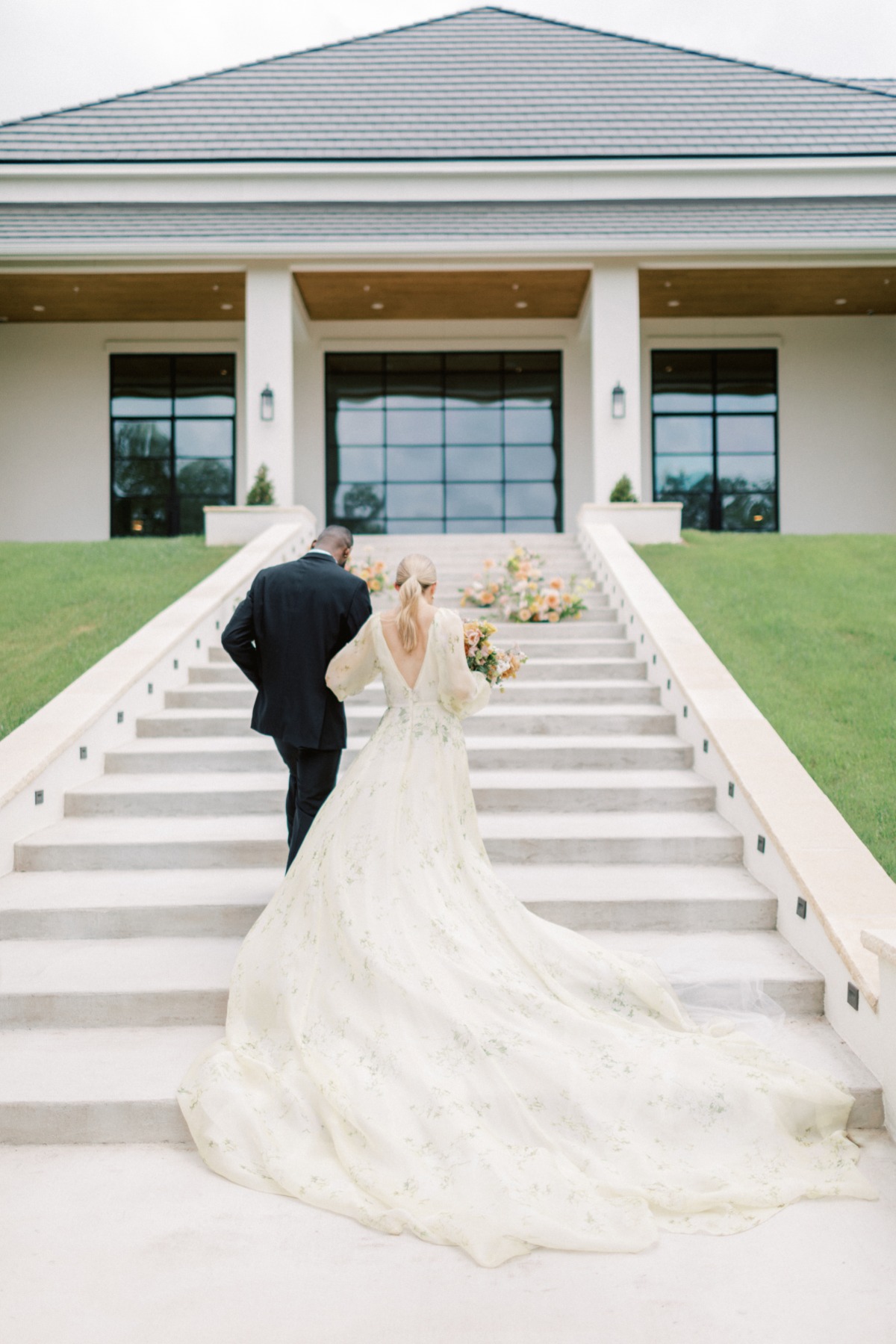 Bride and groom walking away from camera up the steps of venue holding bouquet