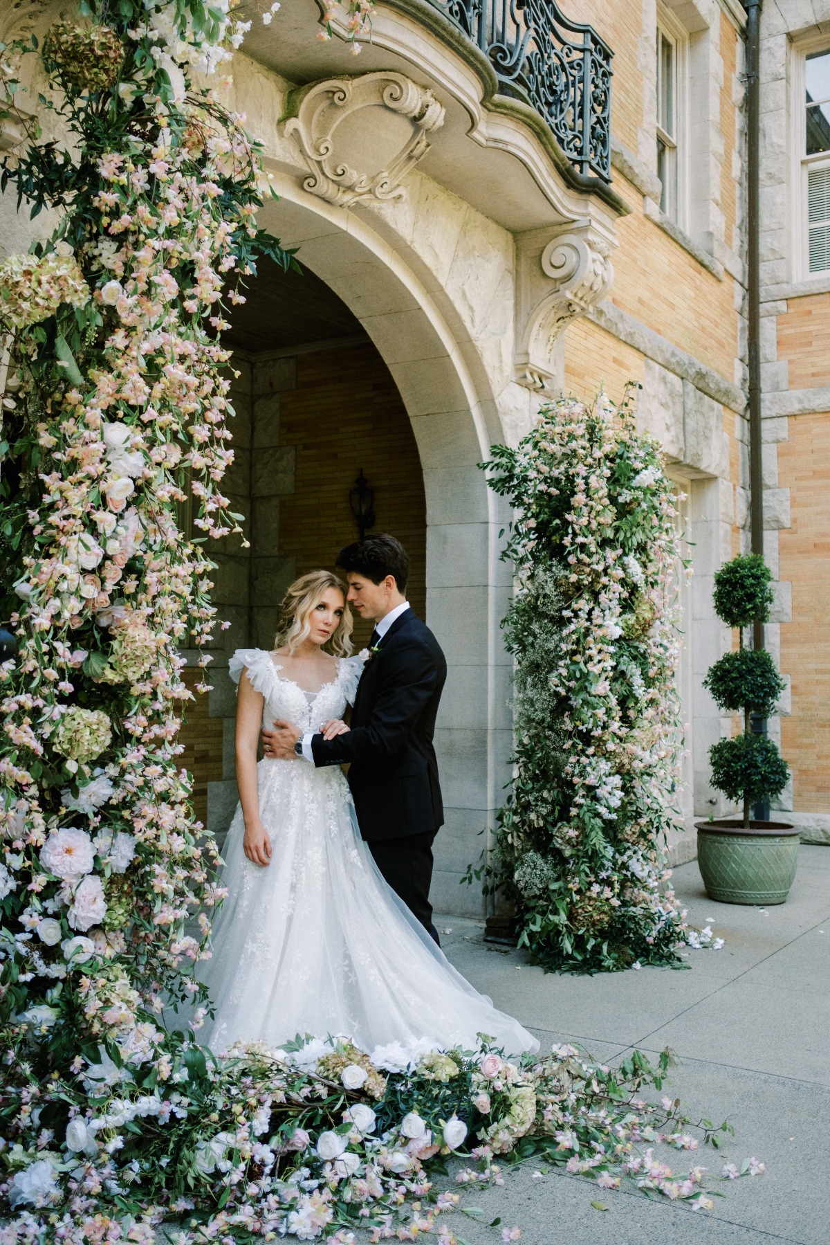 Bride and groom standing together in doorway in front of floral arch