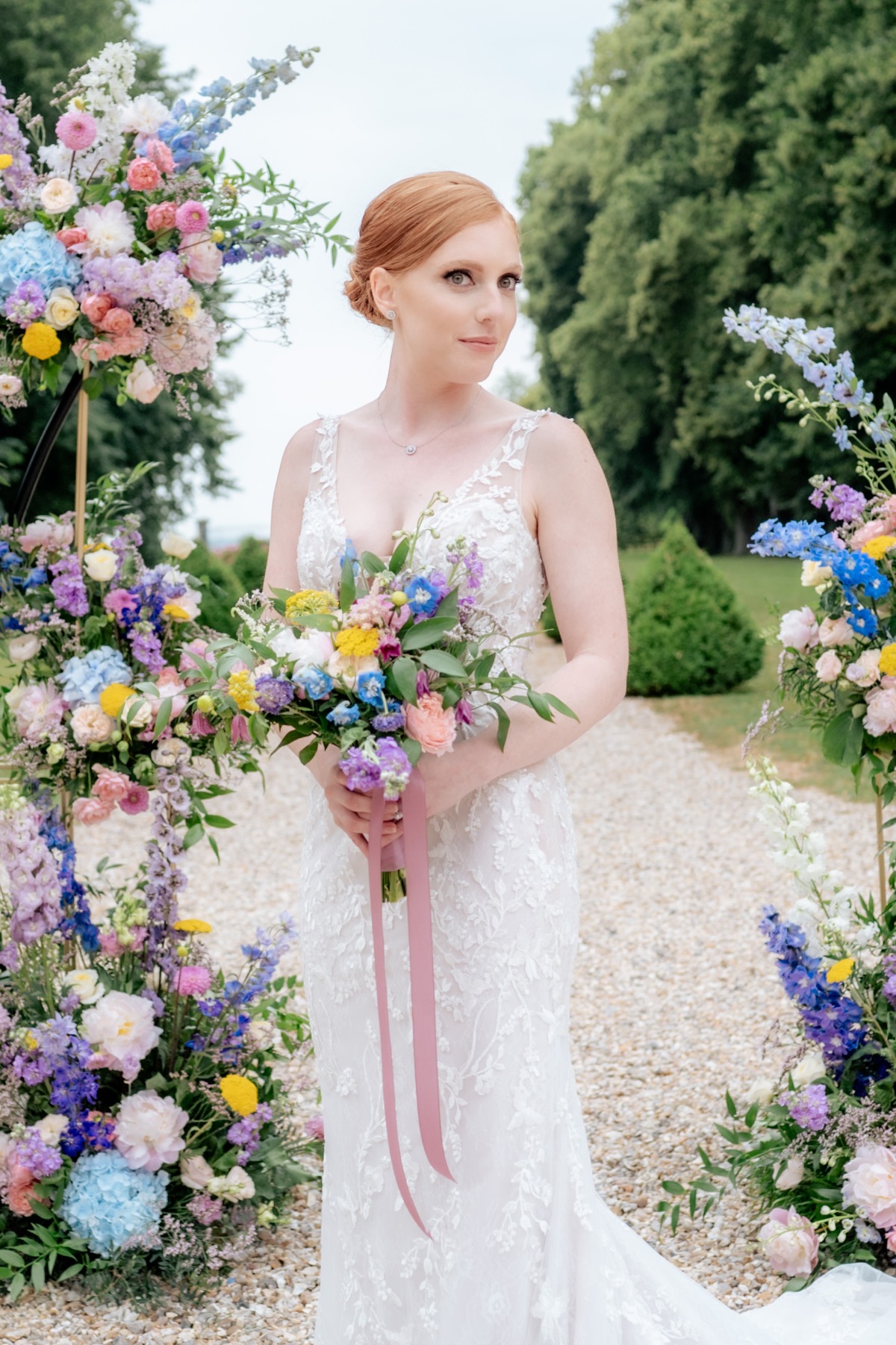 bride poses with bouquet and colorful floral arch in french garden