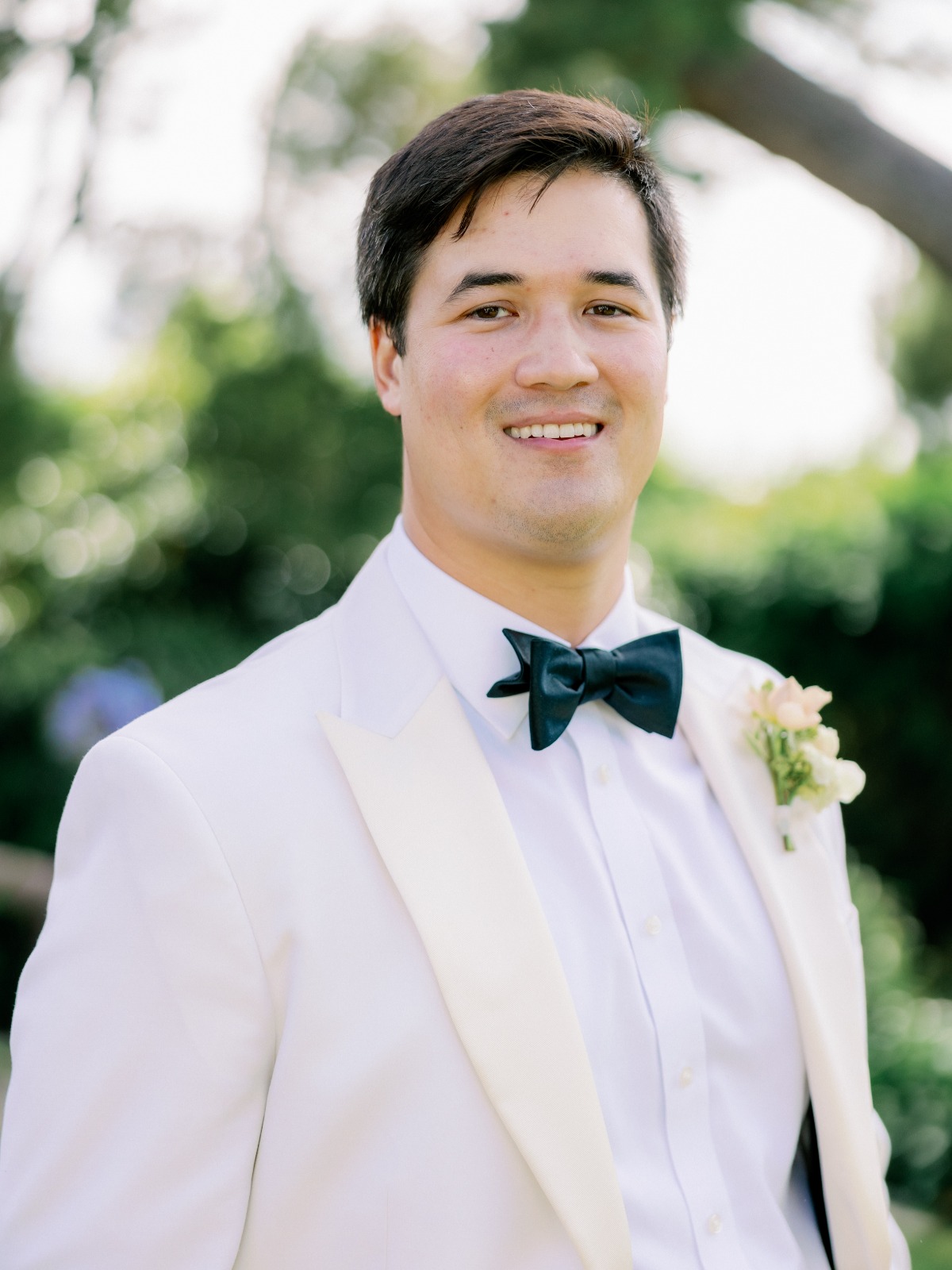 groom in white tuxedo with black bow tie and pastel boutonnière