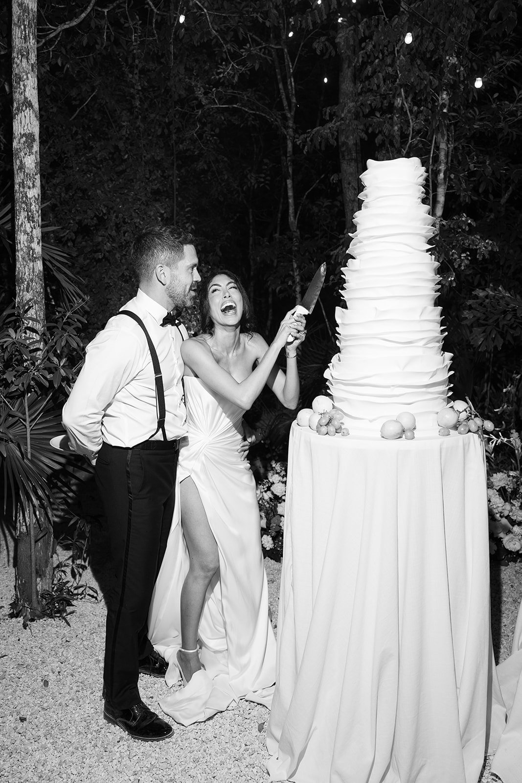 Playful bride cutting giant layered wedding cake in Tulum