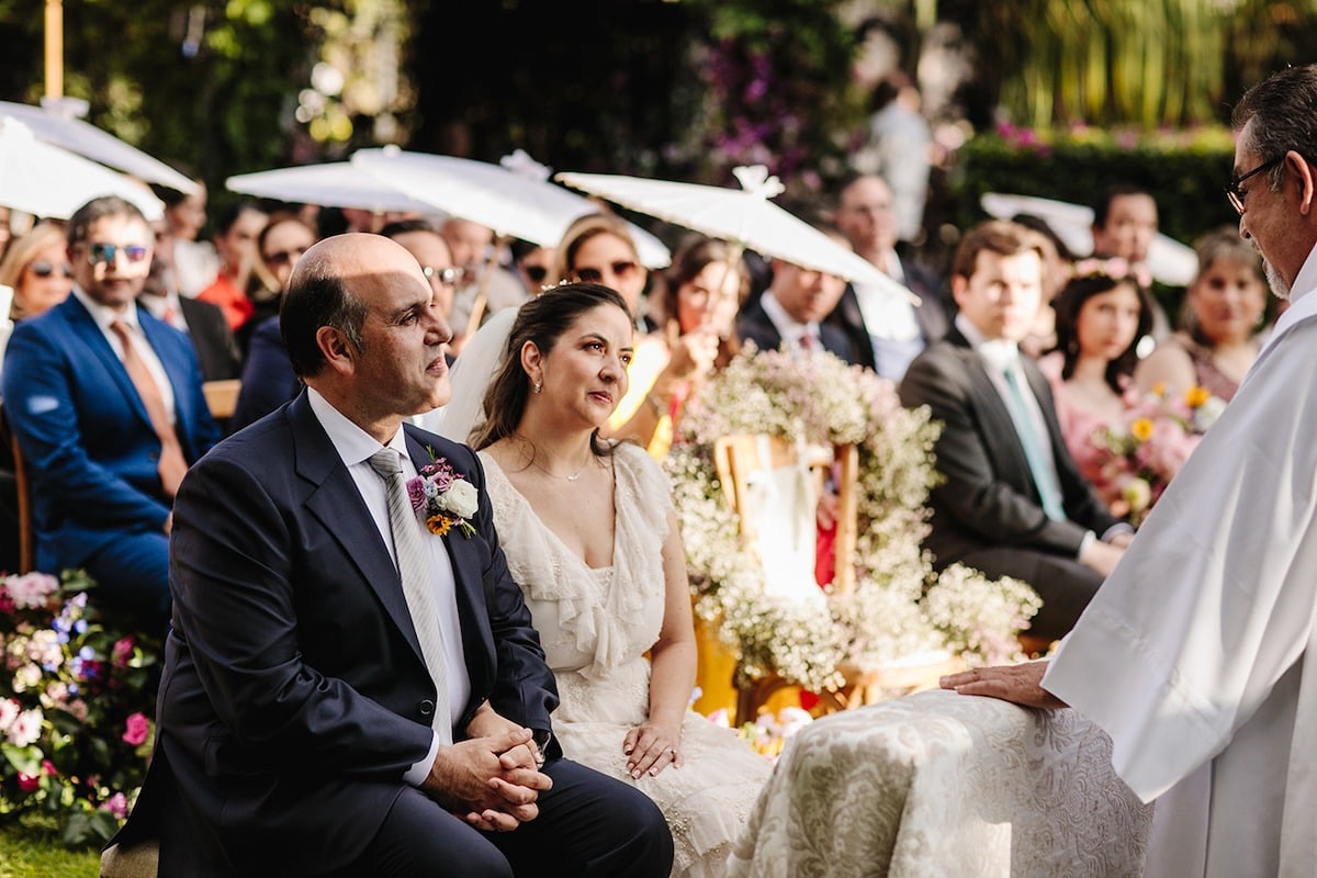 bride and groom sit for outdoor catholic wedding ceremony