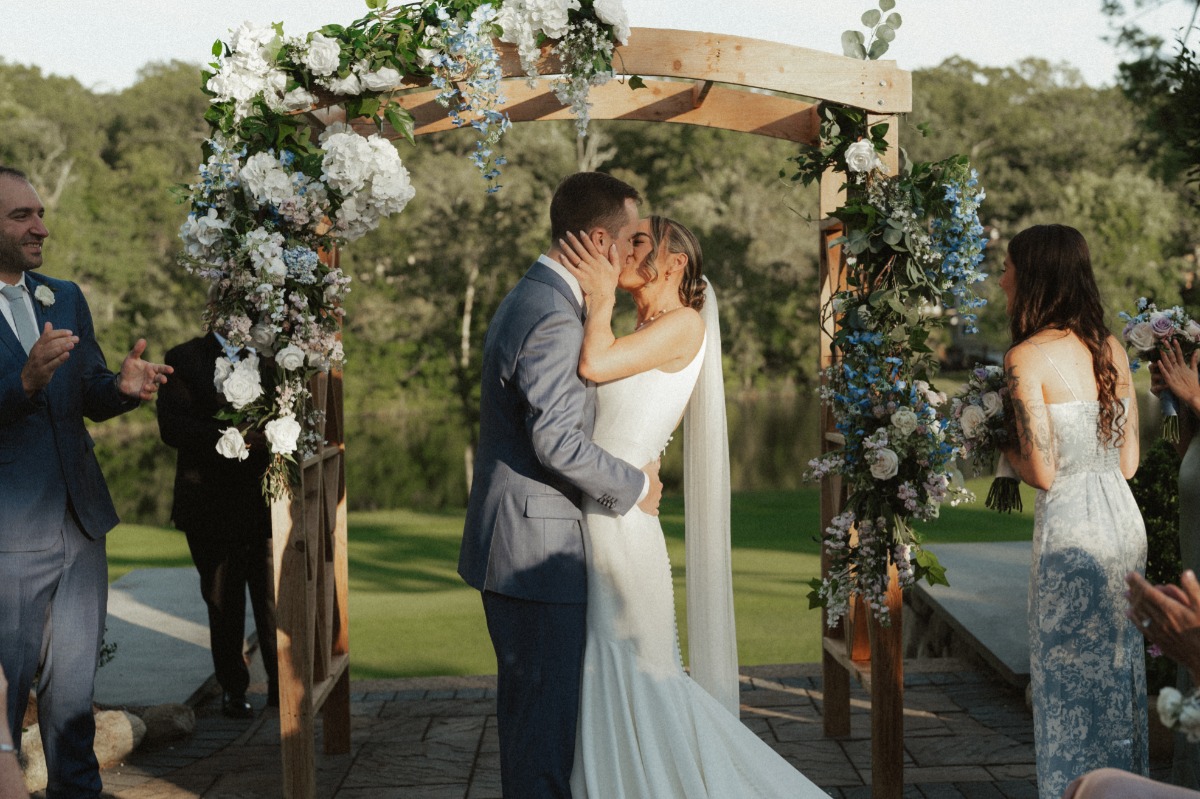 bride and groom kiss at garden wedding with blue and white flowers