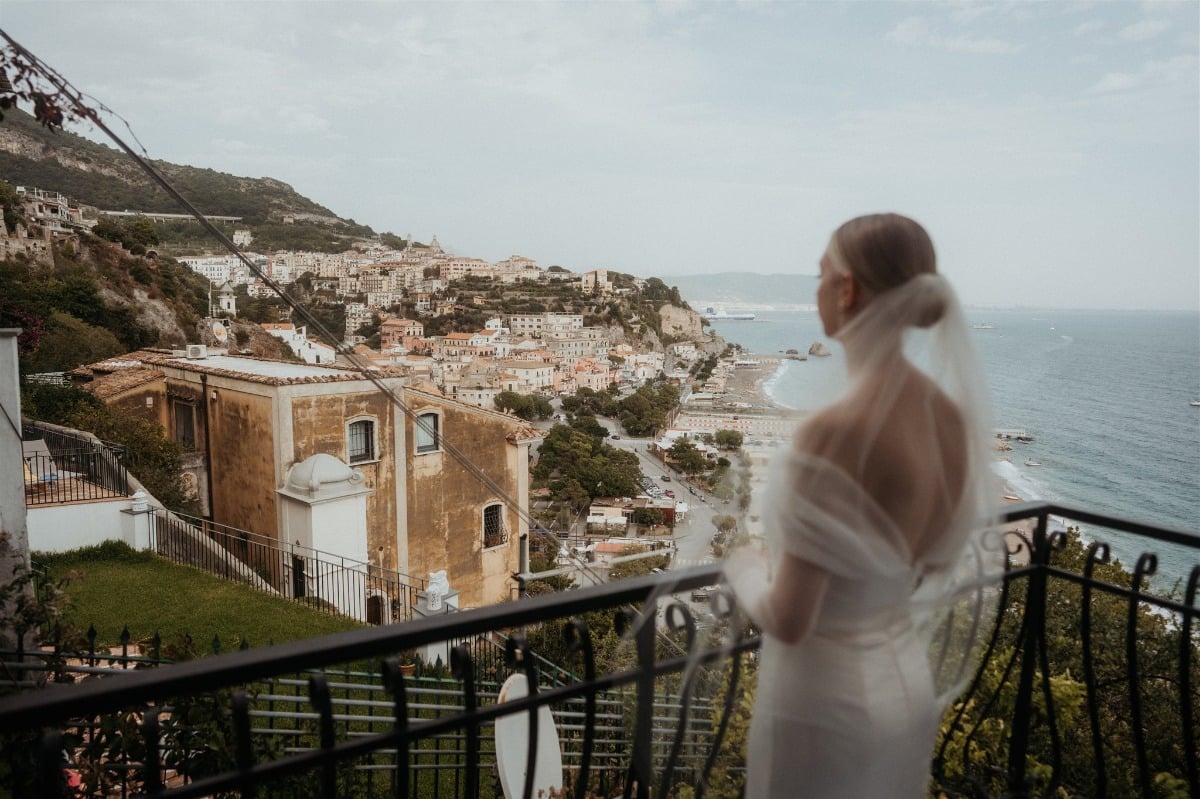 bride in off the shoulder gown looks off of balcony in positano