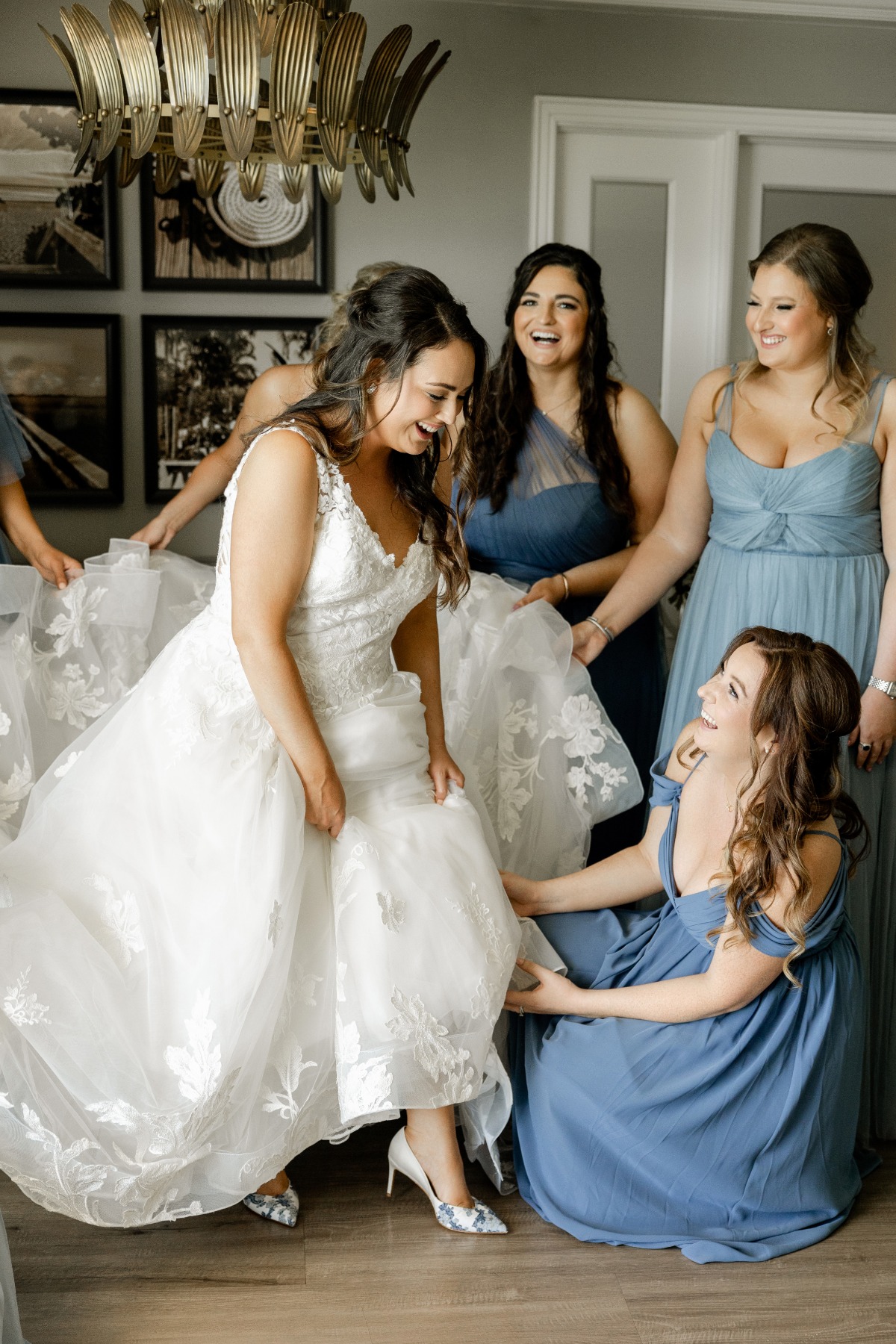 bridesmaids in blue dresses help bride in lace gown