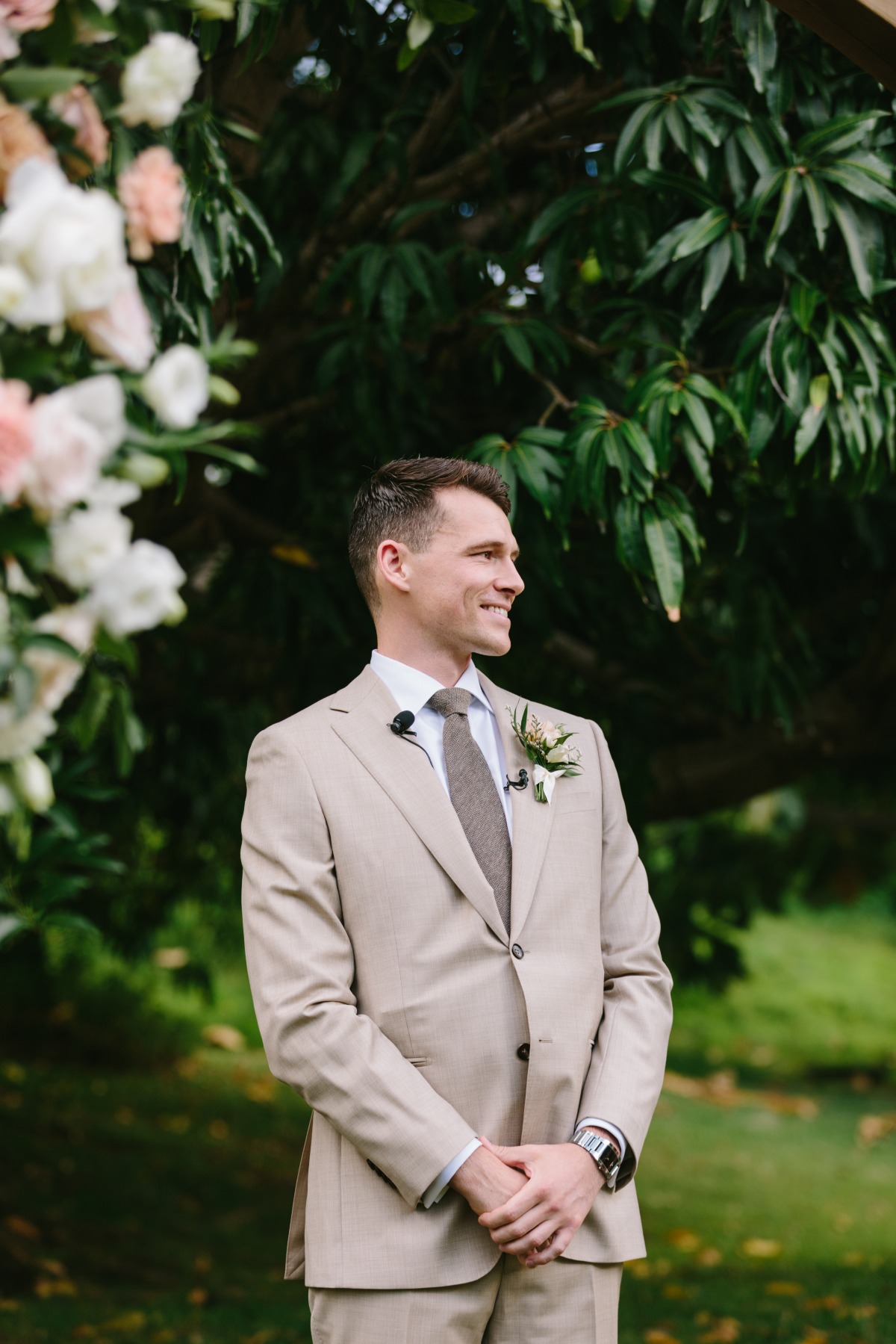 groom in tan suit at tropical wedding ceremony