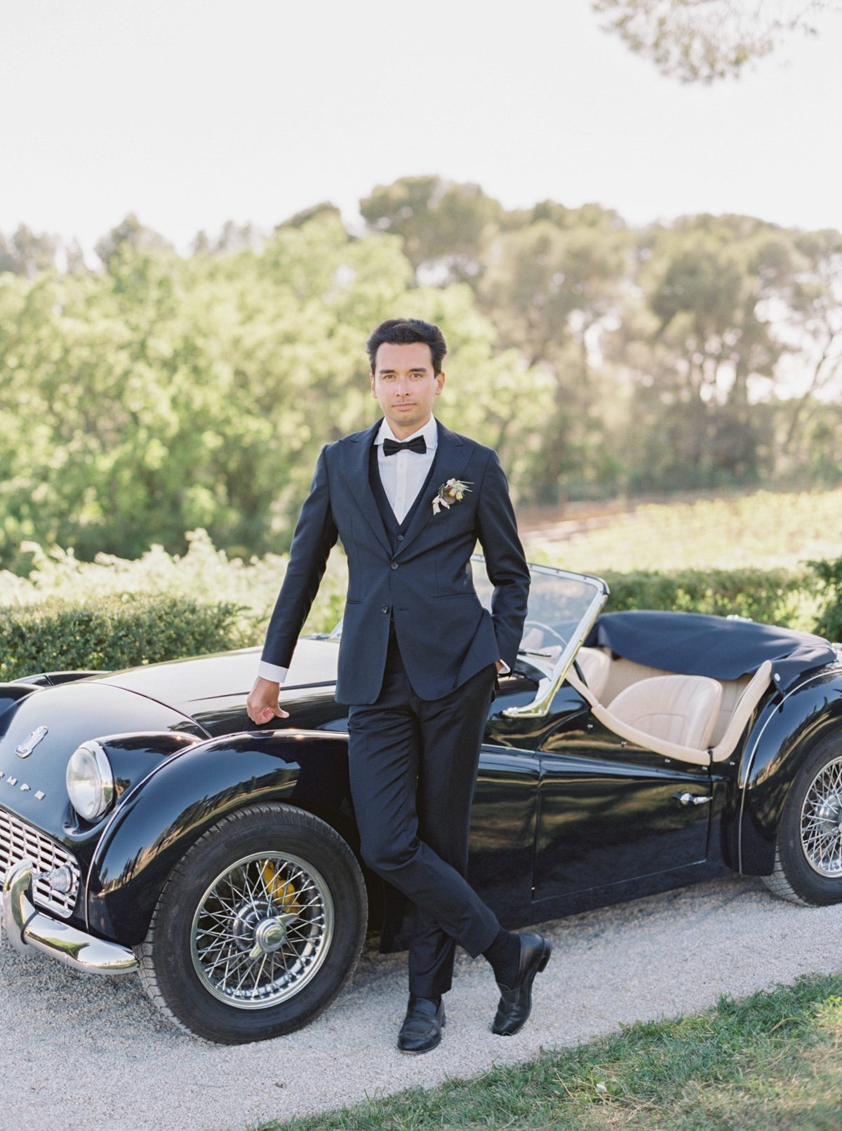 groom in tuxedo by a black vintage car