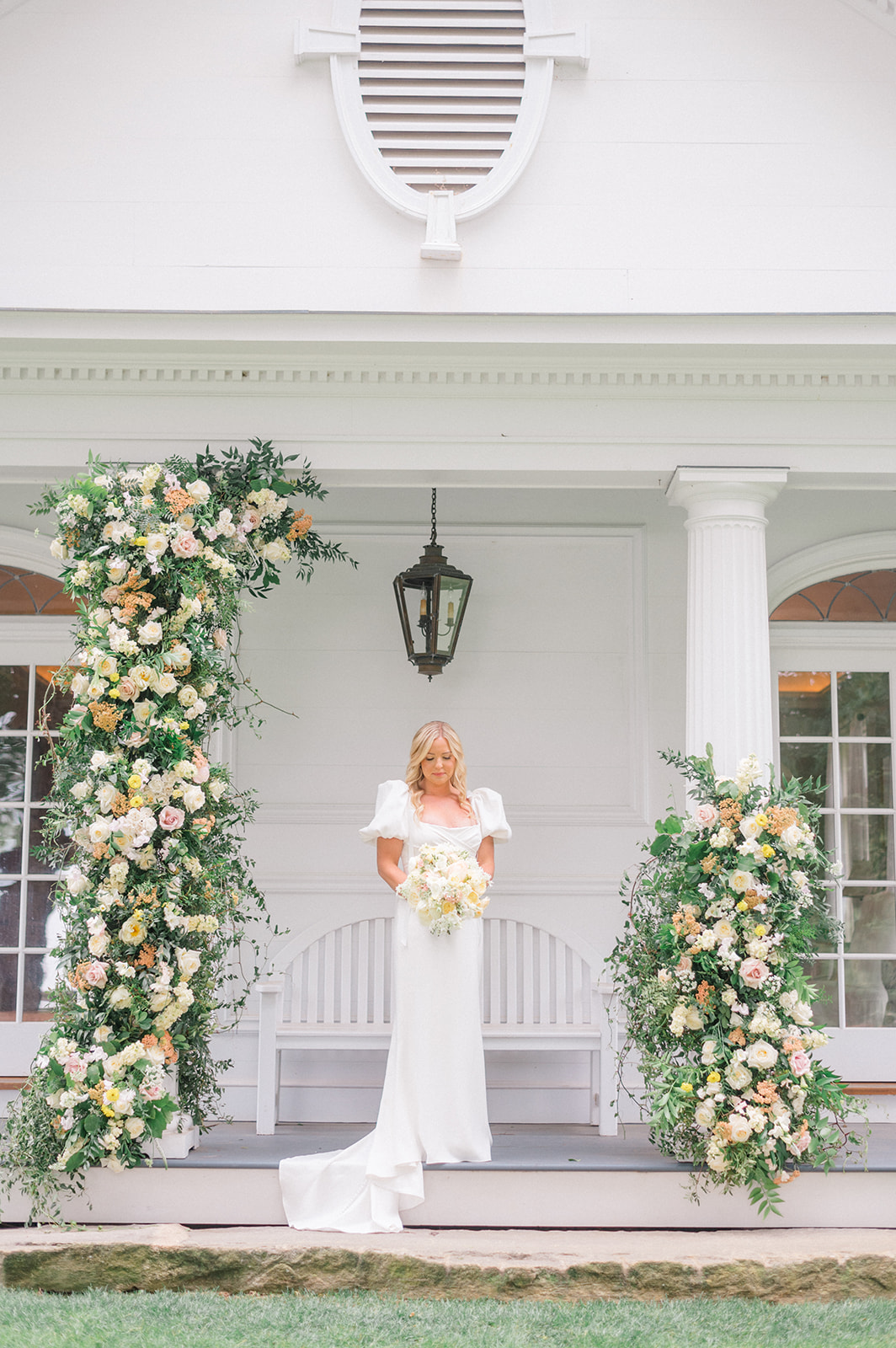 bride poses with bouquet and peach floral arch