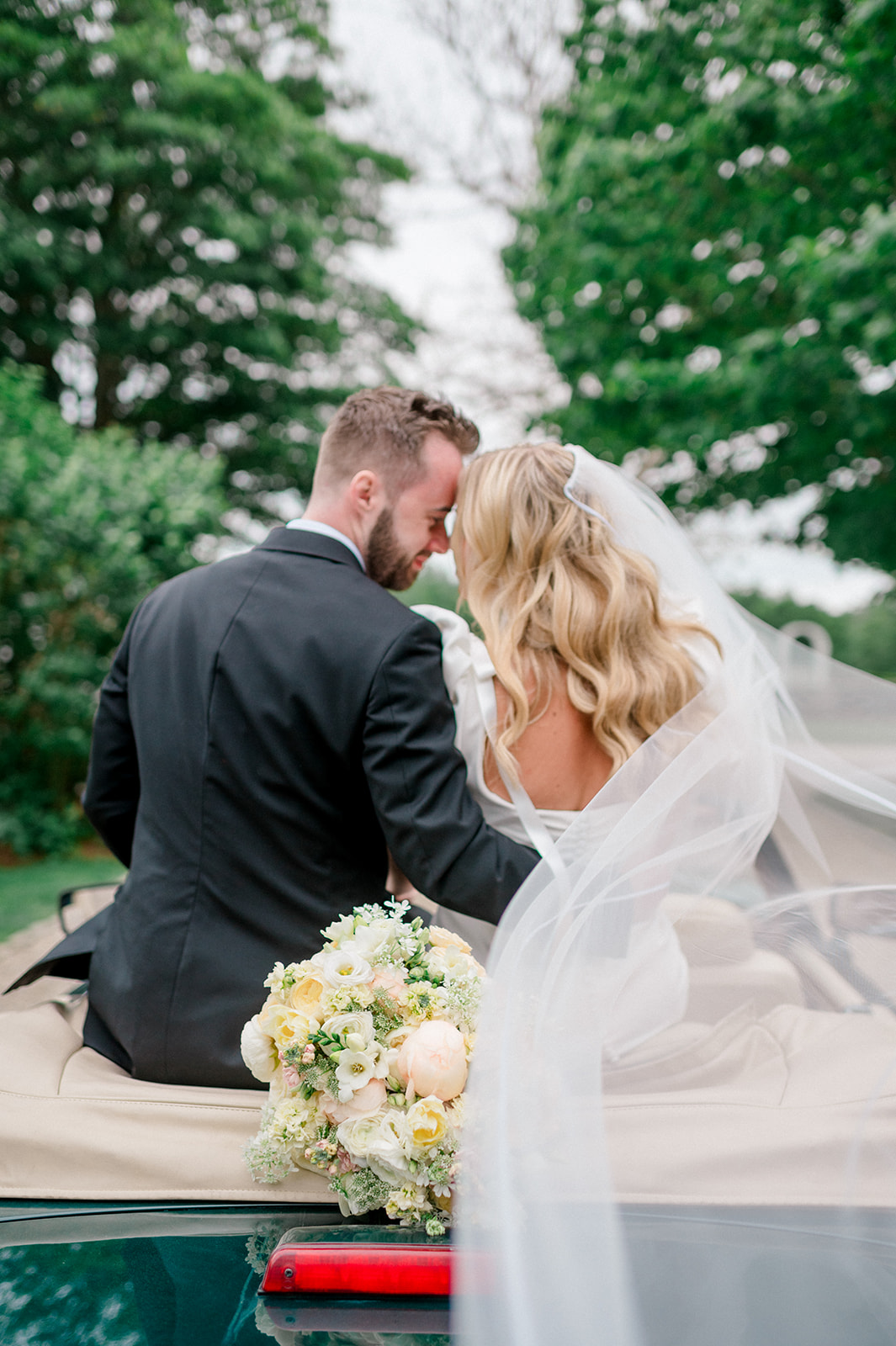 bride and groom in getaway car with veil blowing in the wind