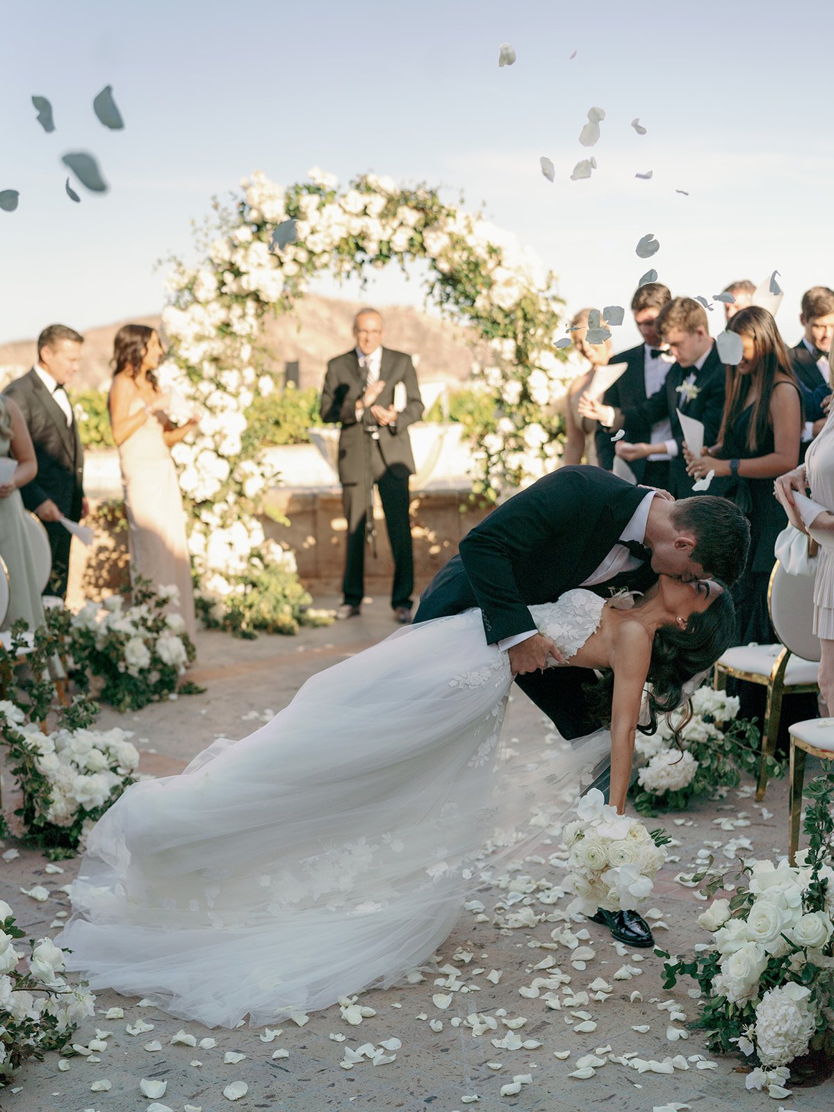 bride and groom kiss at outdoor wedding with petal toss