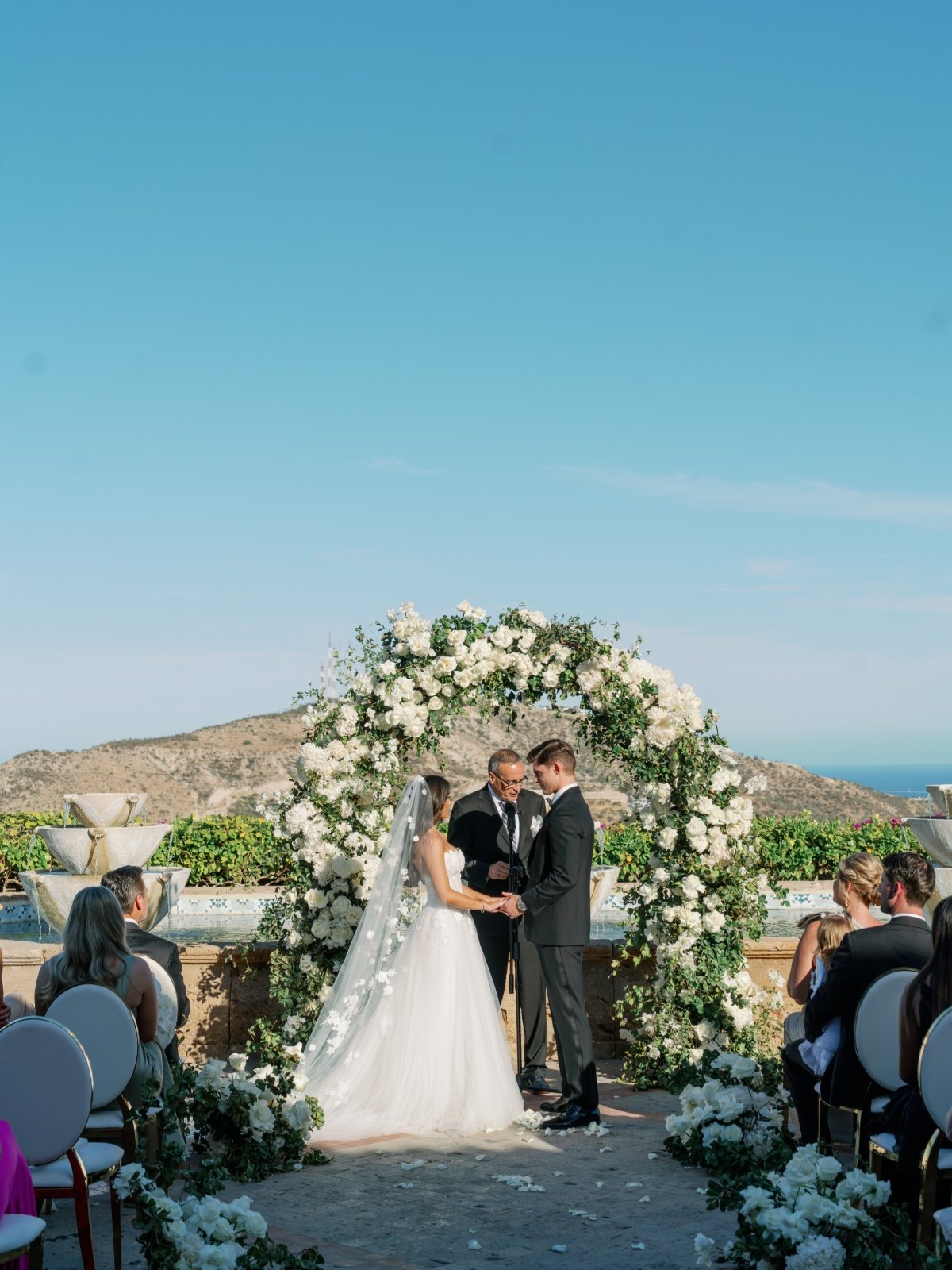 outdoor wedding ceremony in cabo with white rose floral arch