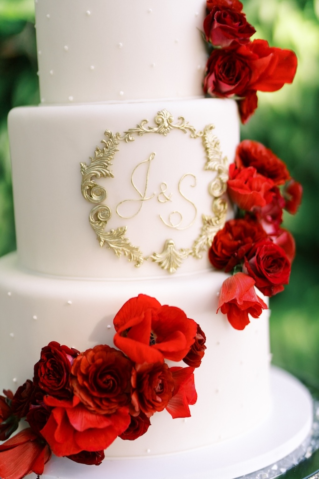 gold monogrammed fondant wedding cake with live red flowers