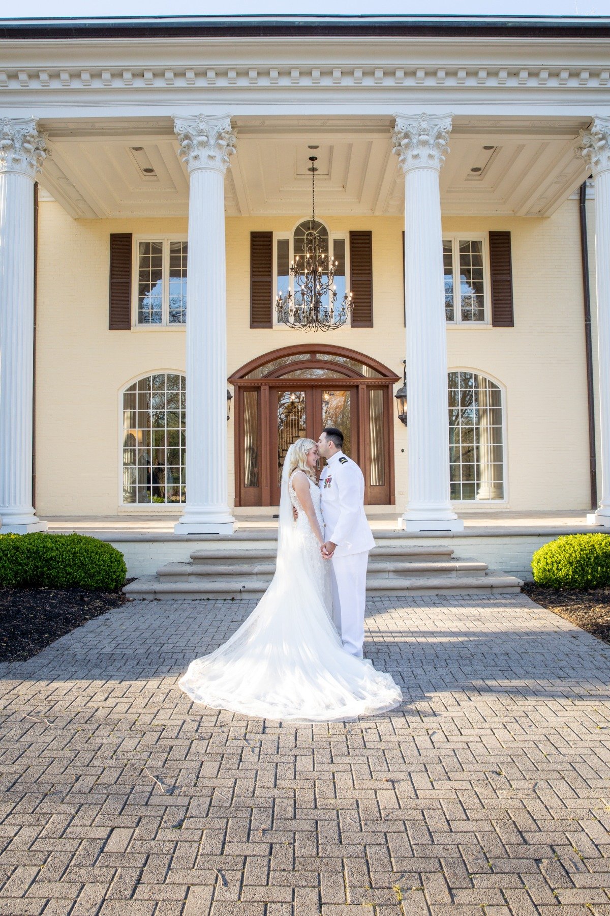 bride and groom in front of estate with pillars