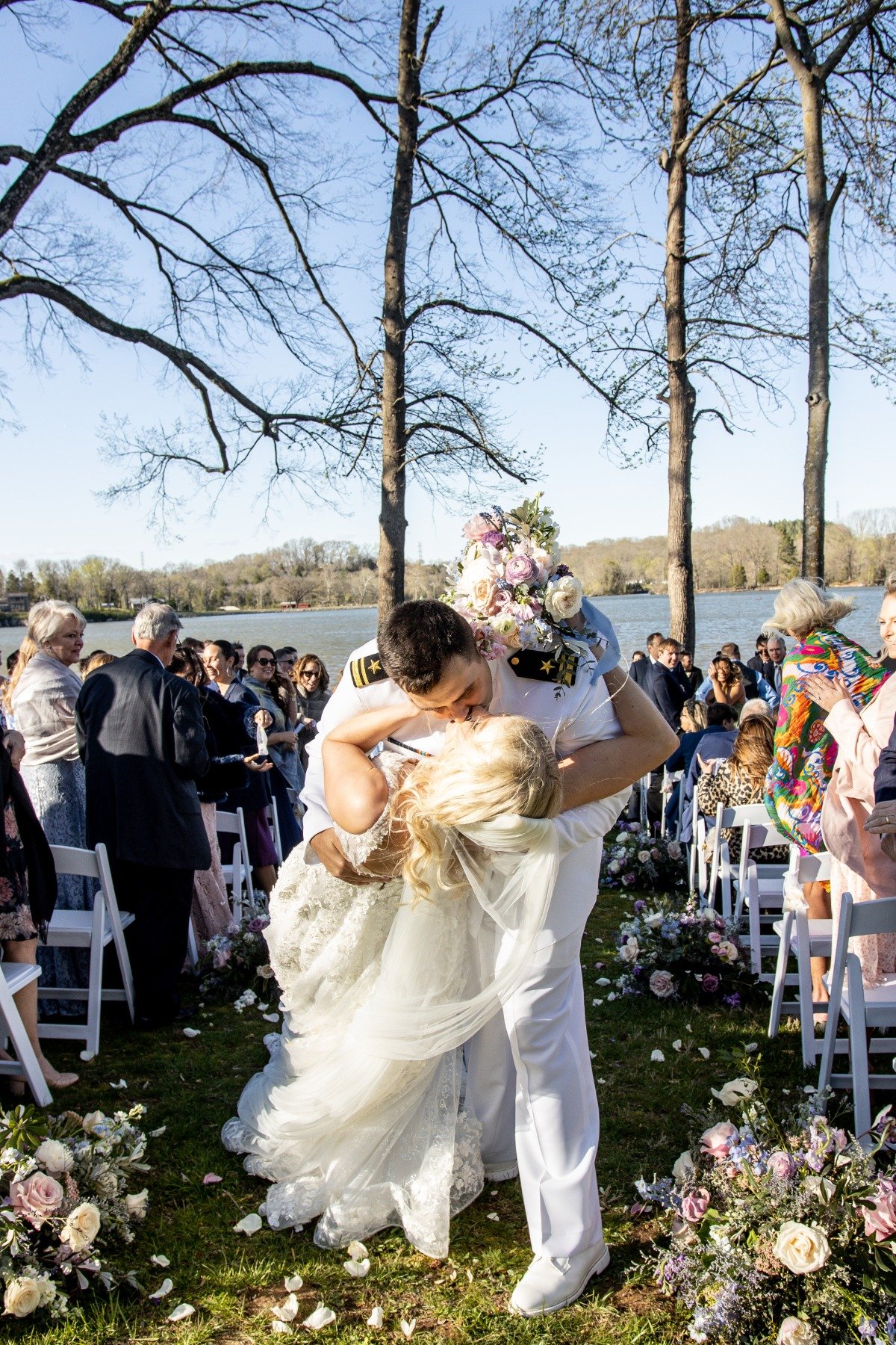 bride and groom kiss at lakefront wedding with rose petal toss