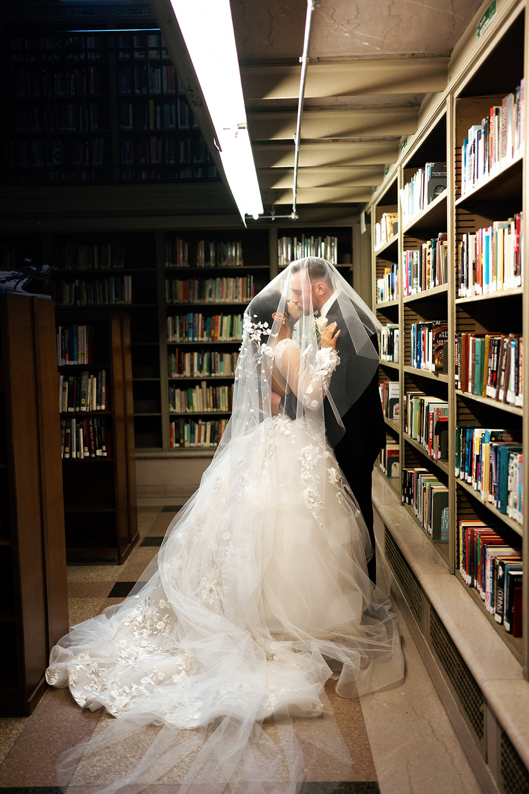 bride and groom kiss among bookshelves