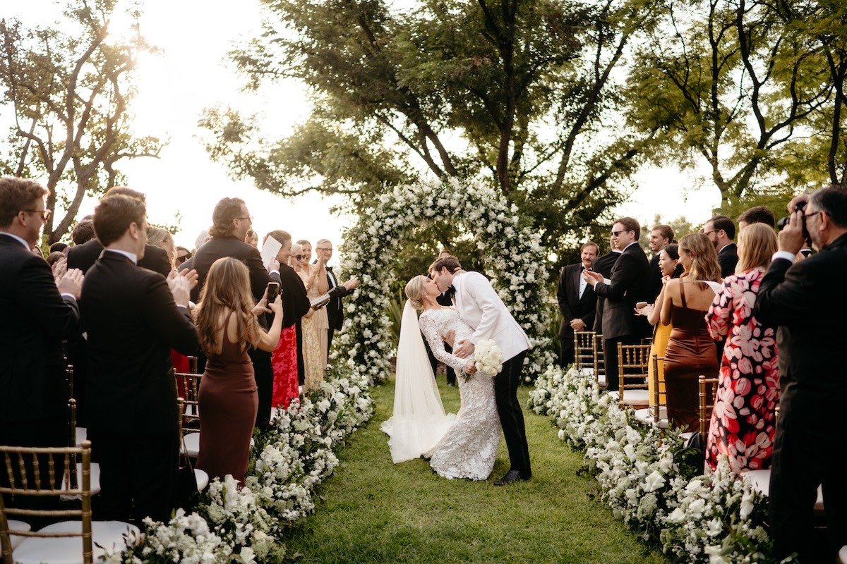 bride and groom kiss at outdoor wedding ceremony with white flowers