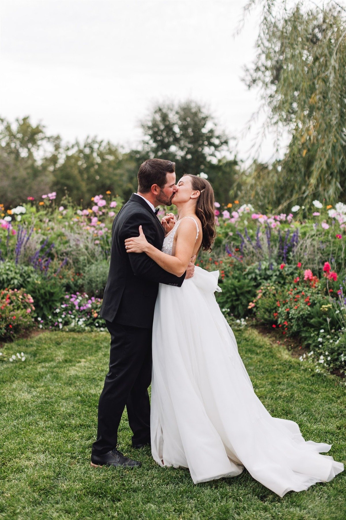 bride and groom kiss in field of wildflowers