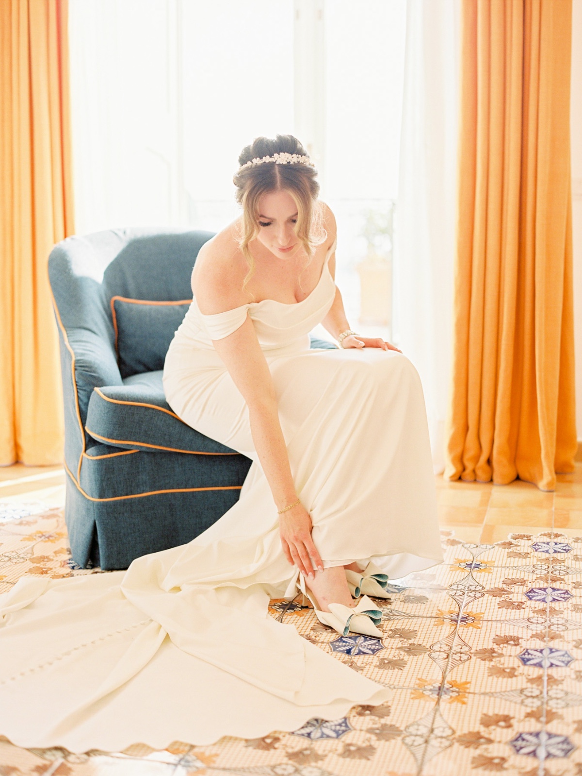 bride in off the shoulder gown putting on pointed wedding shoes