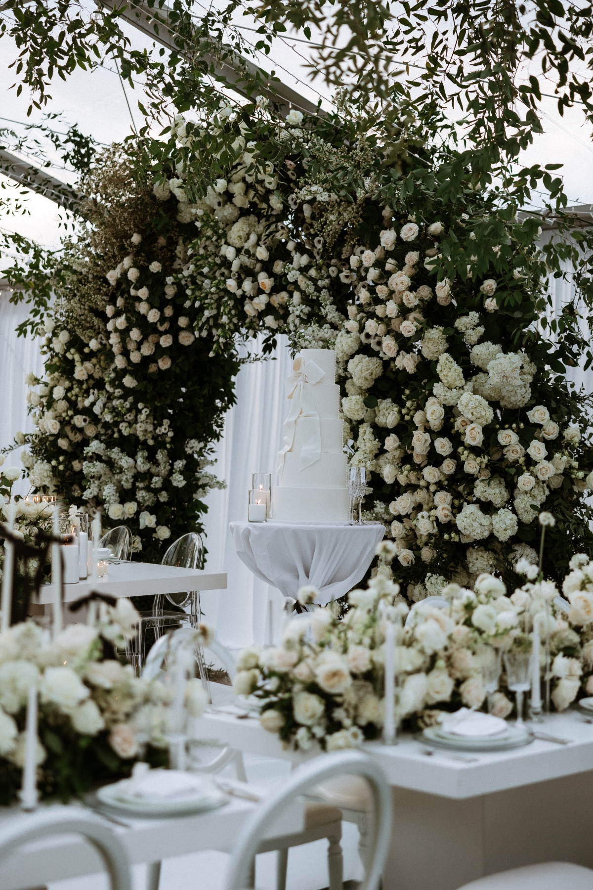 large white wedding cake with bow and flower arch