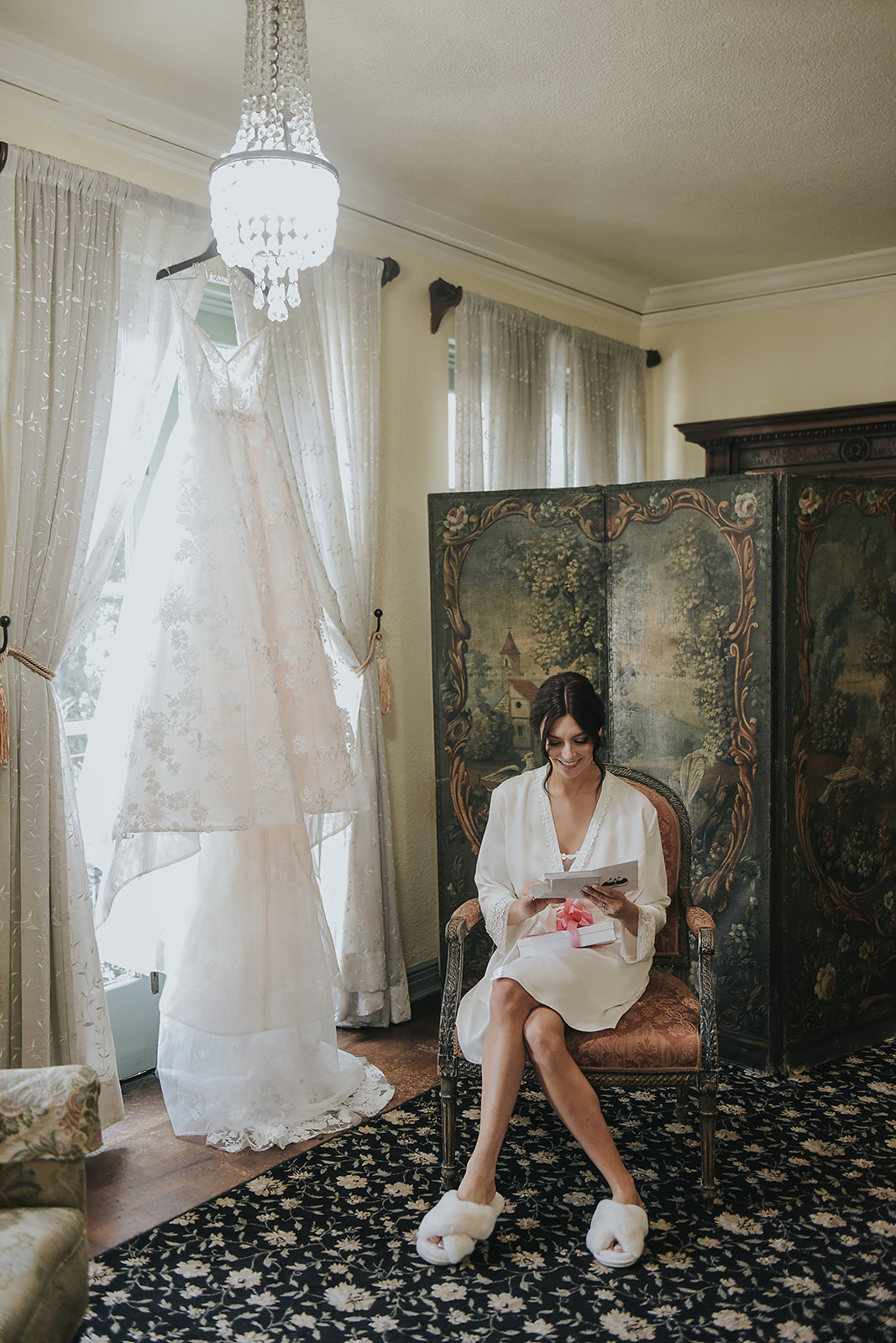 bride getting ready for wedding in silk robe with dress hanging